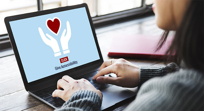 laptop screen showing two hands holding heart with text below that says Give Accessibility