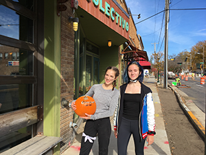 Two female students stand on a sidewalk holding a pumpkin