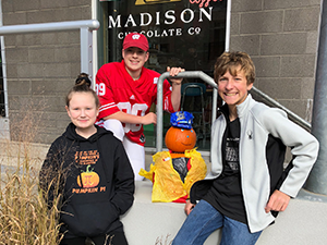 Two male students and one female student stand outside of Madison Chocolate Co with a pumpkin