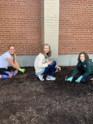 Three happy girls in sixth grade outside planting bulbs