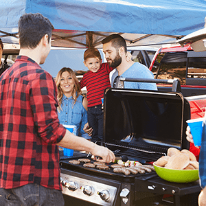 Family stands in front of a man cooking on a grill