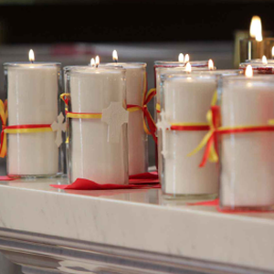 Glowing candles with crosses tied around them sit on a granite surface