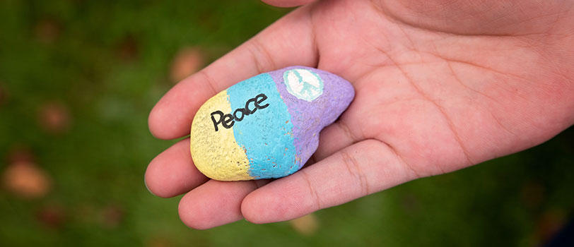 Hand holds a painted rock with the word peace written on it