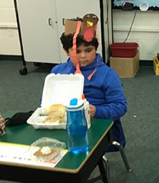 Male student wearing turkey hat and eating thanksgiving meal