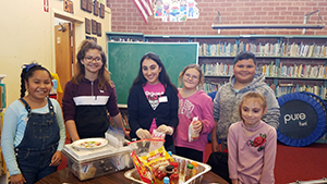 Group of six smiling elementary students standing in front of an activity table