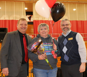 Mrs. Linda standing with two other adults receiving balloons and a bouquet of flowers
