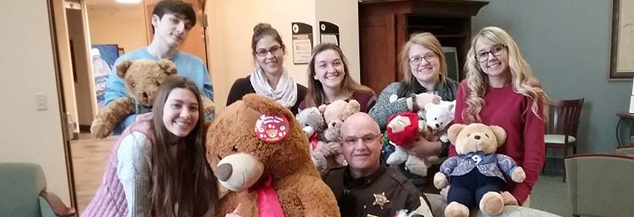 Students and a police officer pose with teddy bears