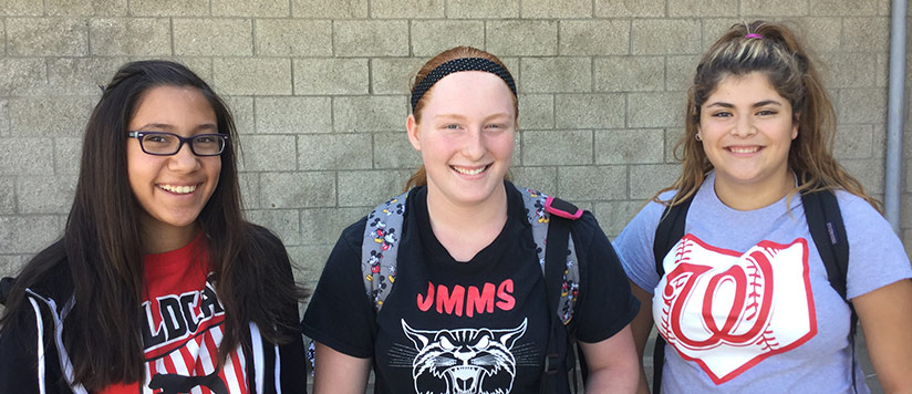 three female students wearing backpacks in front of a brick wall