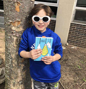 Student holding a book while leaning against a tree