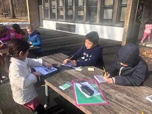 Students reading books outside at a picnic table