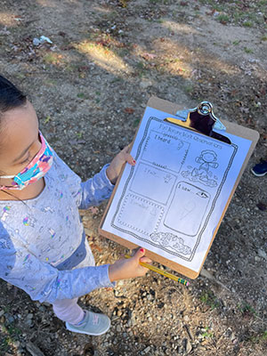 Students showing her clipboard for the camera of her nature observations