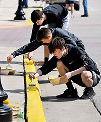 Three male students paint curbs