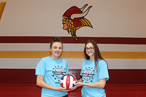 Two female volleyball players holding a ball
