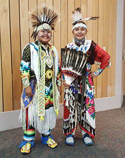 Two students dressed in Native American attire pose and smile together