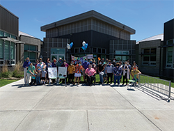 Students, staff and teachers pose together outside with teacher appreciation signs