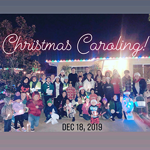 Christmas carolers pose outside of a house with text reading Christmas Caroling Dec 18, 2019