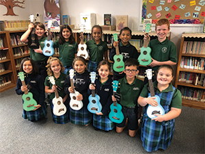 Eleven students pose with ukeleles in a classroom