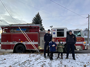 Two fireman with poster winner and brother in front of firetruck