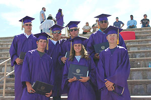 7 students in graduation gowns with diplomas